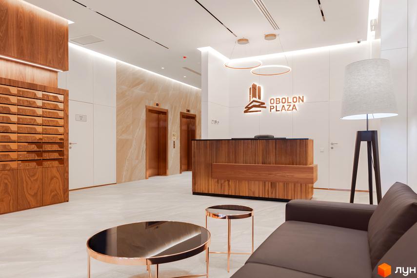 Лобі житлового комплексу Obolon Plaza з ресепшн, ліфтами та зоною відпочинку. Сучасний дизайн інтер'єру з дерев'яними елементами та м'якими меблями.