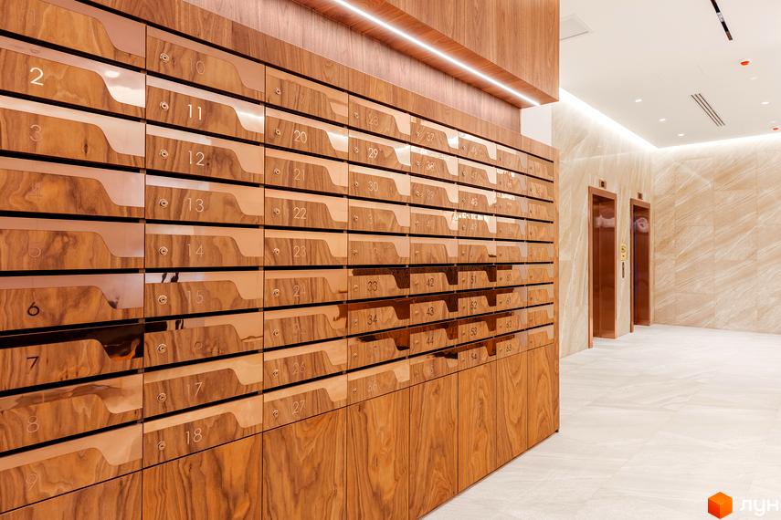 Сучасний дизайн холу житлового комплексу Obolon Plaza з дерев'яними елементами та мідними поштовими скриньками. Поруч розташовані ліфти.