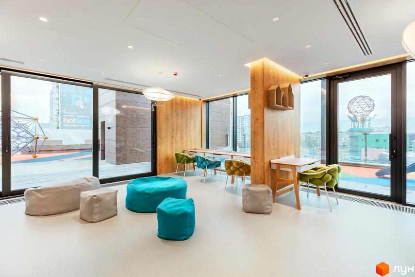 Інтер'єр зони відпочинку в ЖК Obolon Plaza з м'якими меблями та столами біля великих вікон. Навколо зручні крісла та пуфи для комфортного проведення часу.