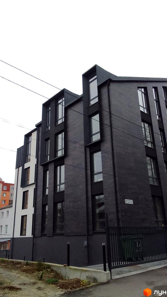 Фасад будинку з чорної цегли та білої штукатурки на вул. Петрушевича, 8. Прибудинкова територія з огорожею та зеленими насадженнями.