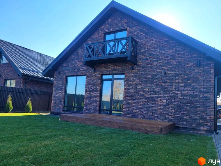 Цегляний будинок з великими вікнами та балконом у Містечку котеджів Зелена Баварія, розташований на доглянутій зеленій галявині.