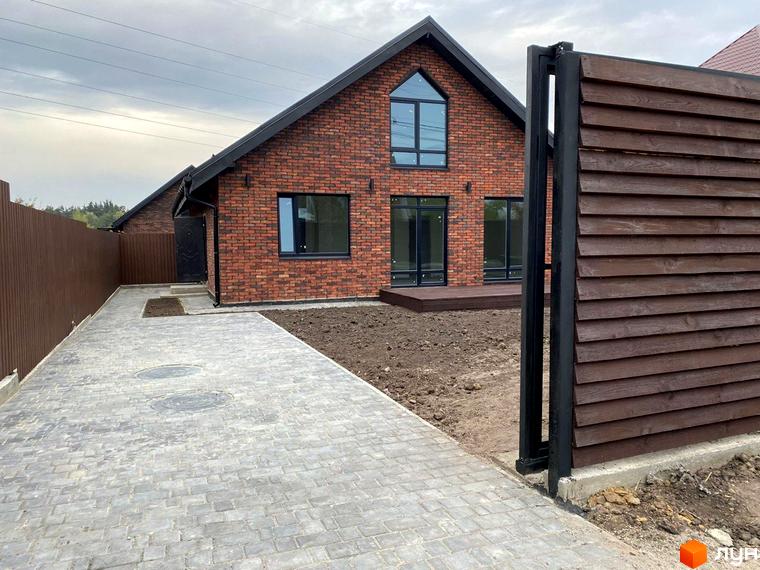 Цегляний будинок з панорамними вікнами та темною покрівлею в Котеджному містечку Зелена Баварія. Бруківка на подвір'ї та дерев'яний паркан.