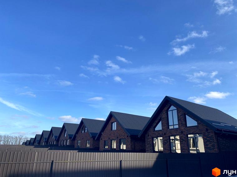 Ряд будинків у Котеджному містечку Південна Баварія з темно-коричневою цегляною кладкою та темною покрівлею на тлі блакитного неба.