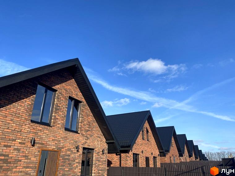 Цегляні будинки з чорними дахами в Котеджне містечко Південна Баварія на фоні блакитного неба. Видно паркан та частину прибудинкової території.