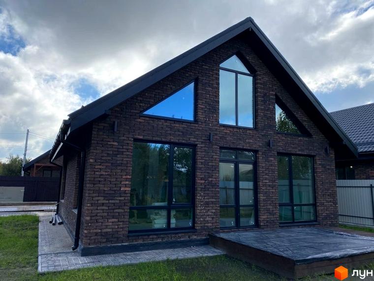 Цегляний будинок з великими вікнами та чорним дахом в Котеджному містечку Південна Баварія. На передньому плані газон та тераса.