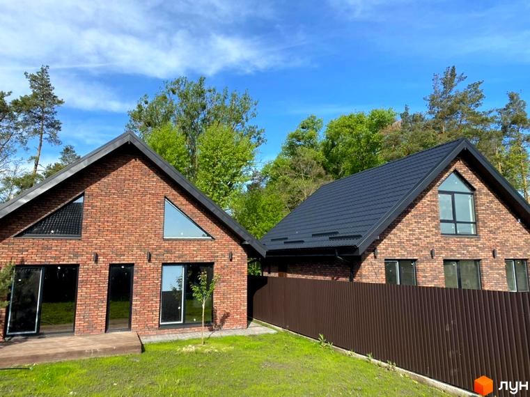 Два будинки з коричневої цегли з чорним дахом та великими вікнами. Перед будинками зелена трава та дерева, а також коричневий паркан.