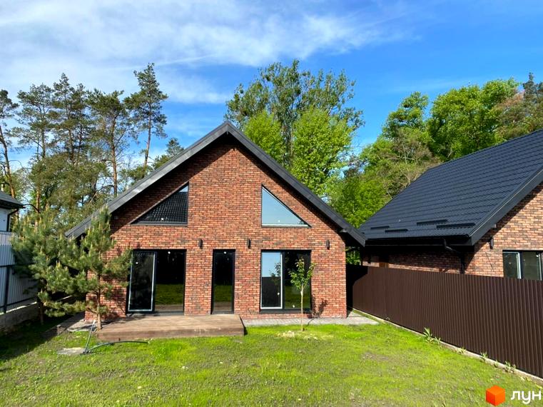 Цегляний будинок з трикутними вікнами та чорним дахом в Котеджному містечку Південна Баварія. На подвір'ї газон та дерева, сонячна погода.