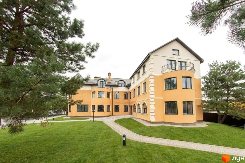 Житловий комплекс Мюнхен: триповерхова будівля з жовтою та білою обробкою, балконами та великими вікнами, оточена доглянутим зеленим газоном та деревами.