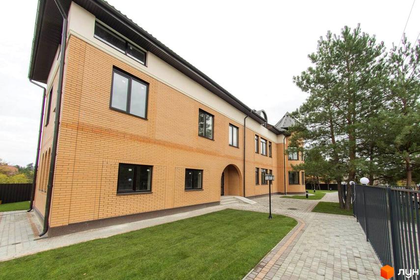 Житловий комплекс Мюнхен: двоповерхова будівля з жовтої цегли з чорними вікнами та прибудинковою територією з бруківки та газону.