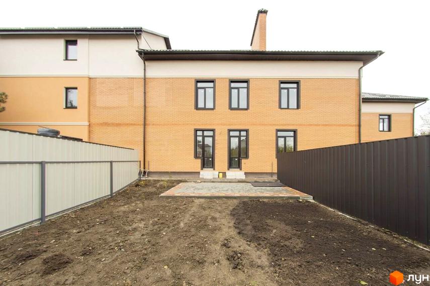 Будинок житлового комплексу Мюнхен з цегляним фасадом та вікнами, огороджений парканом. Прибудинкова територія з плиткою та ґрунтом.