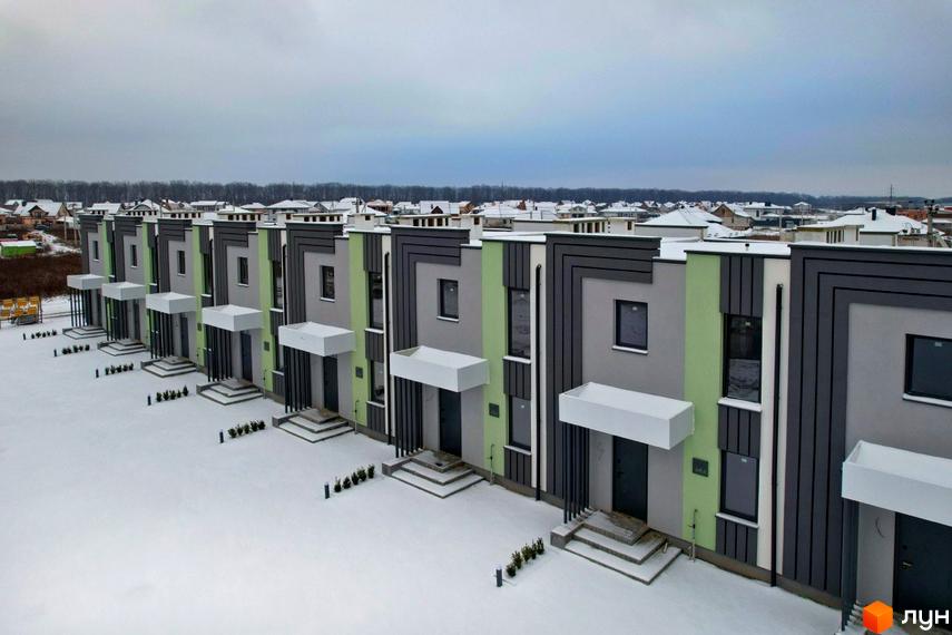 Ряд таунхаусів Green Home з сіро-зеленими фасадами та темними вікнами. Прибудинкова територія вкрита снігом, видно невеликі рослини біля входів.