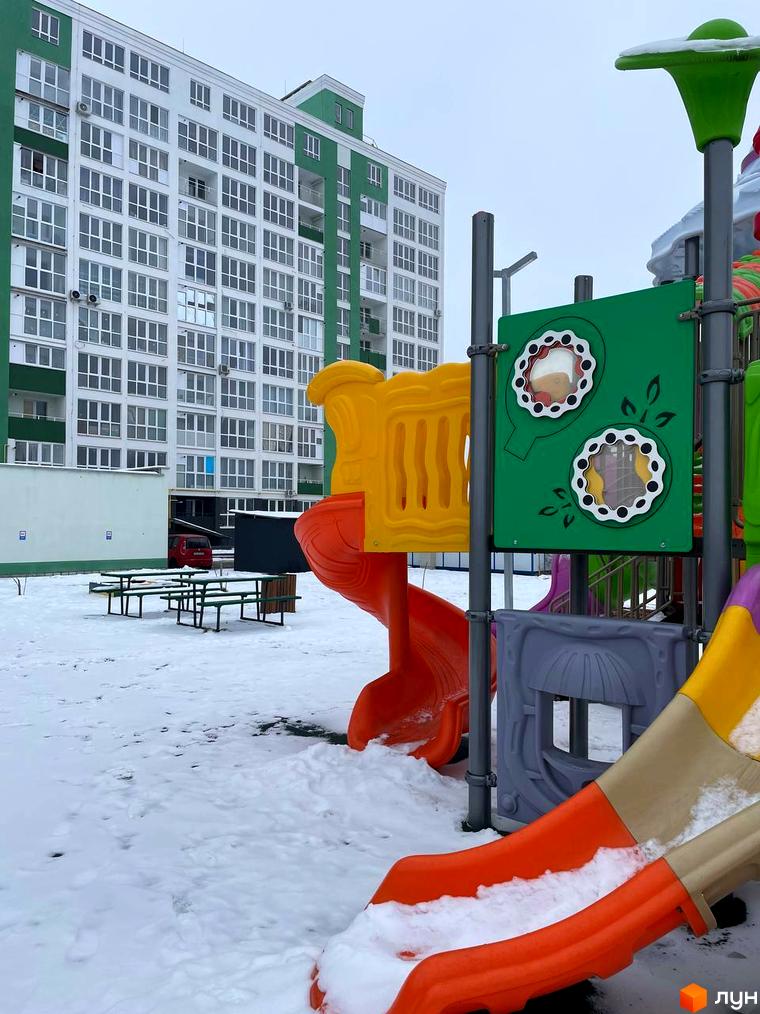 Житловий комплекс Олександрівський з білими фасадами та зеленими вставками. На території дитячий майданчик, вкритий снігом.
