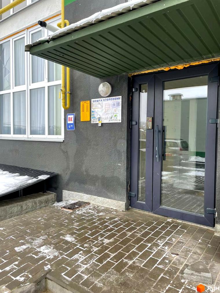 Вхід до будинку з скляними дверима та кодовим замком. Передня частина будинку викладена бруківкою, на якій лежить сніг.