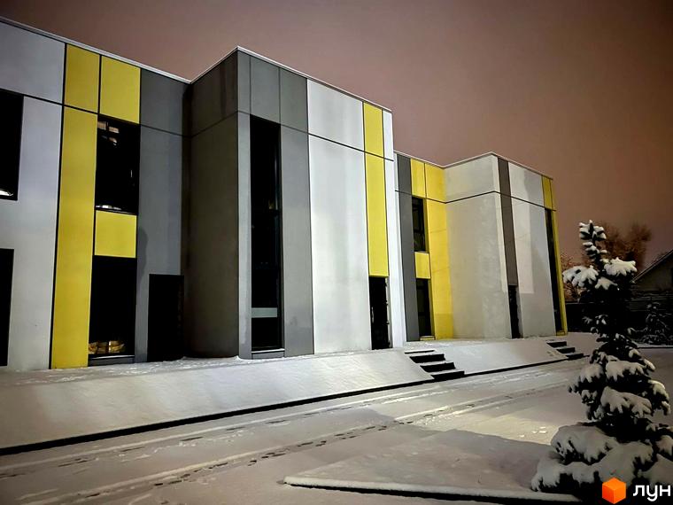 Зимовий вигляд будівлі ЖК ART HOUSE з жовтими та сірими панелями на фасаді. Перед будівлею засніжена прибудинкова територія та ялинка.