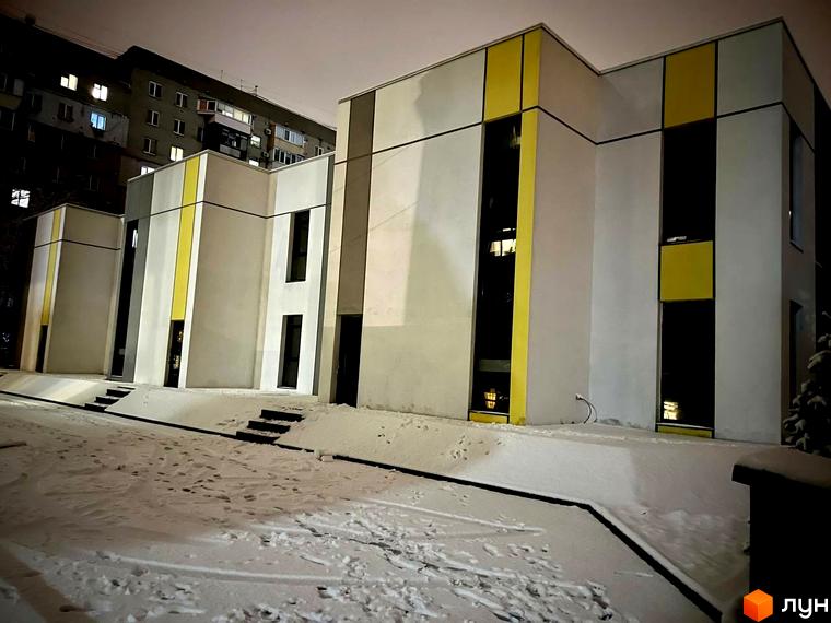 Фасад клубного будинку ART HOUSE з білими стінами та жовтими вставками. Перед будинком сніг, вдалині видно багатоквартирний будинок.