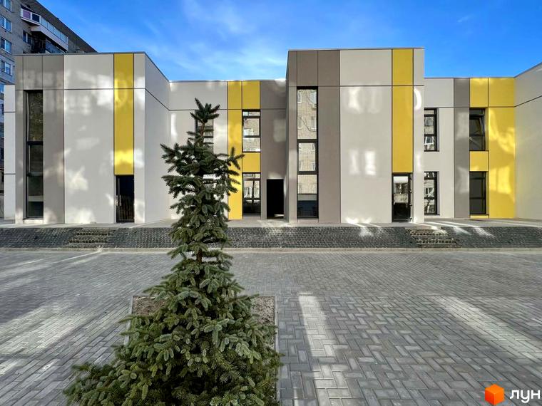 Фасад будівлі Клубний будинок ART HOUSE з жовтими та сірими панелями. Перед будівлею викладена тротуарна плитка та росте ялинка.