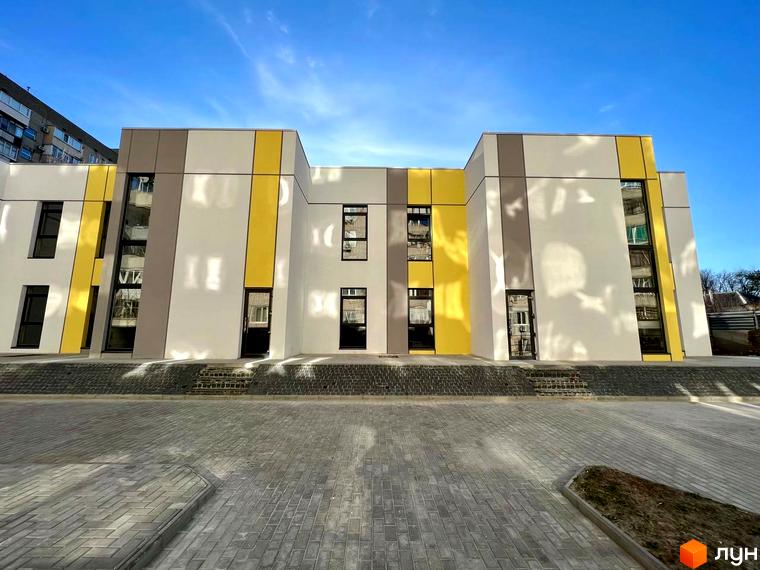 Фасад Клубного будинку ART HOUSE з жовто-сірими вставками, чорними вікнами та дверима. Перед будинком тротуарна плитка.