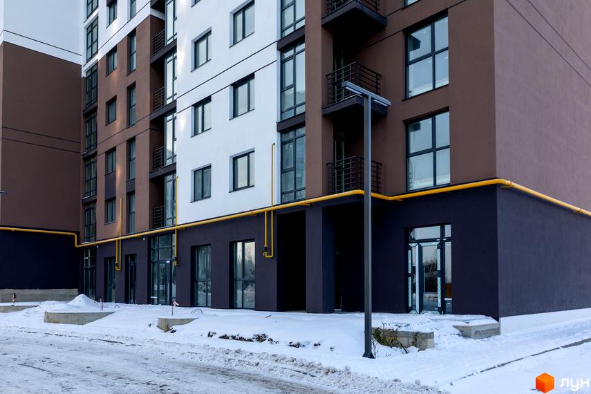 Новобудова ЖК Супернова. Зовнішній вигляд будинку з коричневими та білими фасадами, балконами та жовтими комунікаціями на тлі засніженої території.