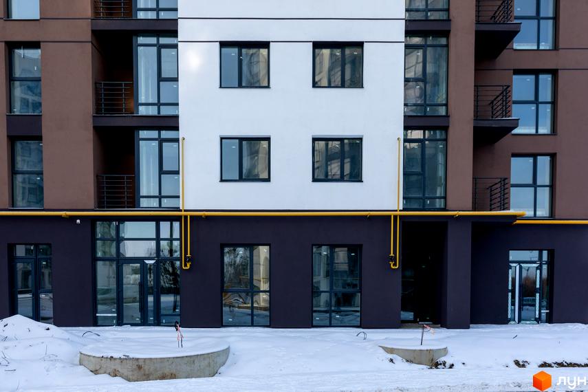 Новобудова ЖК Супернова: фасади з коричневими та білими секціями, великі вікна, балкони, жовті комунікації. Навколо будинку засніжена територія з бетонними елементами.