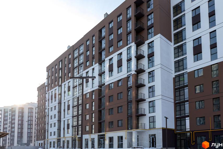 Фасад житлового комплексу Супернова з коричневими та білими секціями, великою кількістю вікон та балконів. Навколо видно інші новобудови та елементи інфраструктури.
