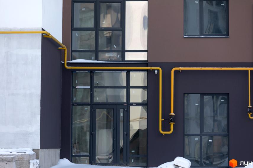 Зовнішній вигляд новобудови ЖК Супернова з великими вікнами та жовтими газовими трубами. Навколо будівлі видно сніг та елементи прибудинкової території.