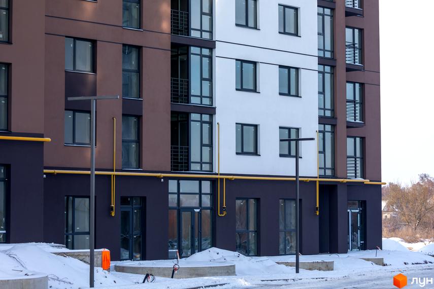 Фасад житлового комплексу Супернова з коричневими та білими секціями, великими вікнами та балконами. Навколо новобудови видно сніг та елементи благоустрою.