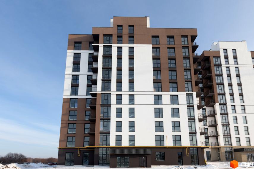 Фасад житлового комплексу Супернова з коричнево-білими елементами та великою кількістю вікон. Навколо будинку видно засніжену територію та дерева.