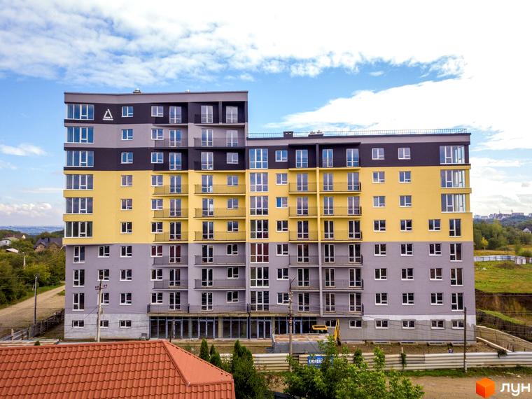 Житловий комплекс Зелені Пагорби: багатоповерховий будинок з жовтими, сірими та чорними фасадами, оточений зеленню.