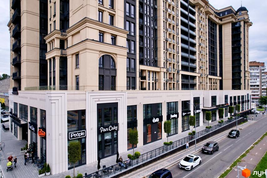 Житловий комплекс Premier Tower з бежевим фасадом та темними вікнами. На першому поверсі розташовані комерційні приміщення та пішохідна зона з деревами.