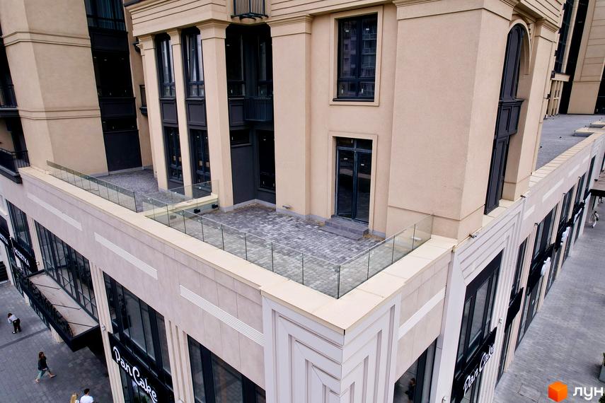 Фасад Житлового комплексу Premier Tower світлого кольору з темними вікнами. На терасі бруківка та скляні перила, внизу пішохідна зона.