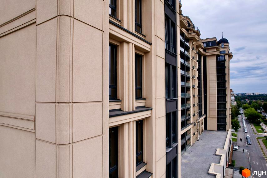 Фасад житлового комплексу Premier Tower світло-бежевого кольору з темними вікнами та декоративними елементами. Видно дорогу та дерева.