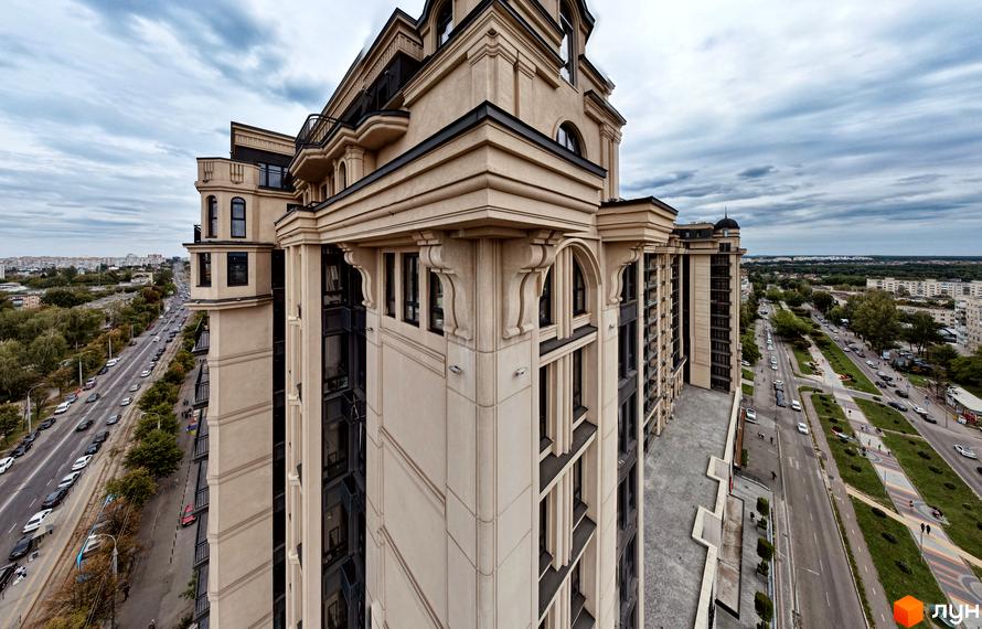 Житловий комплекс Premier Tower: високий будинок з бежевим фасадом та класичними елементами. Поруч дорога з автомобілями та зелені насадження.