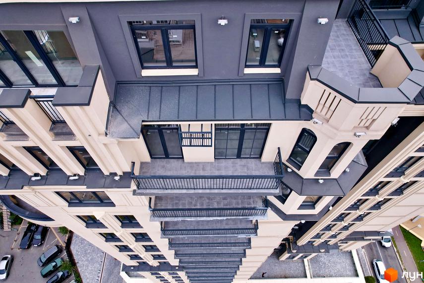 Багатоповерховий будинок Житлового комплексу Premier Tower зі світлим фасадом, темними вікнами та численними балконами. Поруч видно парковку з автомобілями.