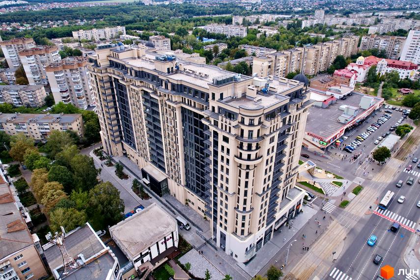 Житловий комплекс Premier Tower: багатоповерхова будівля зі світлим фасадом та темними вікнами, оточена зеленню, дорогою та комерційними об'єктами.