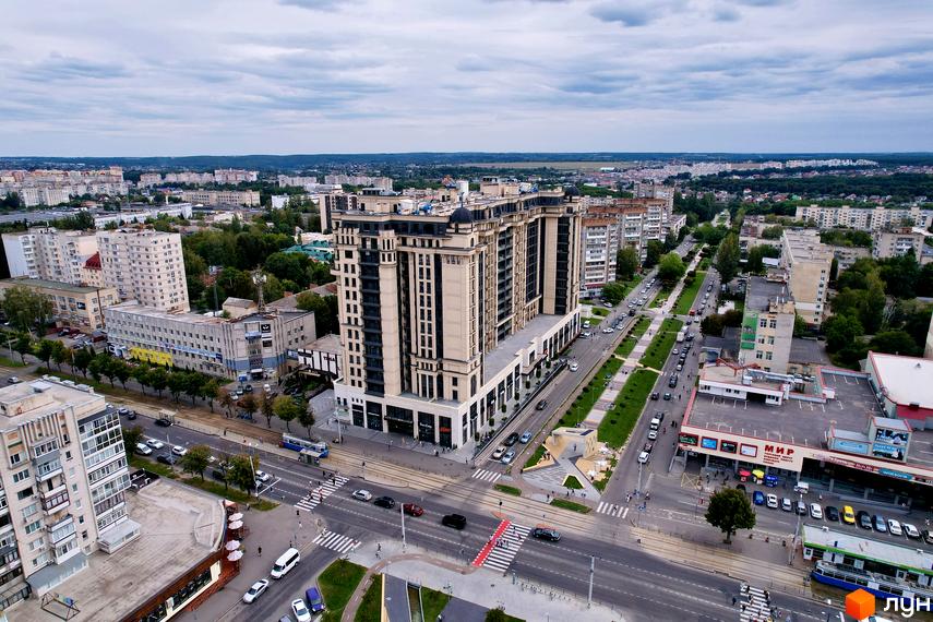 Житловий комплекс Premier Tower світлого кольору з темними вікнами, розташований біля широкої вулиці з трамвайною лінією та зеленими насадженнями.