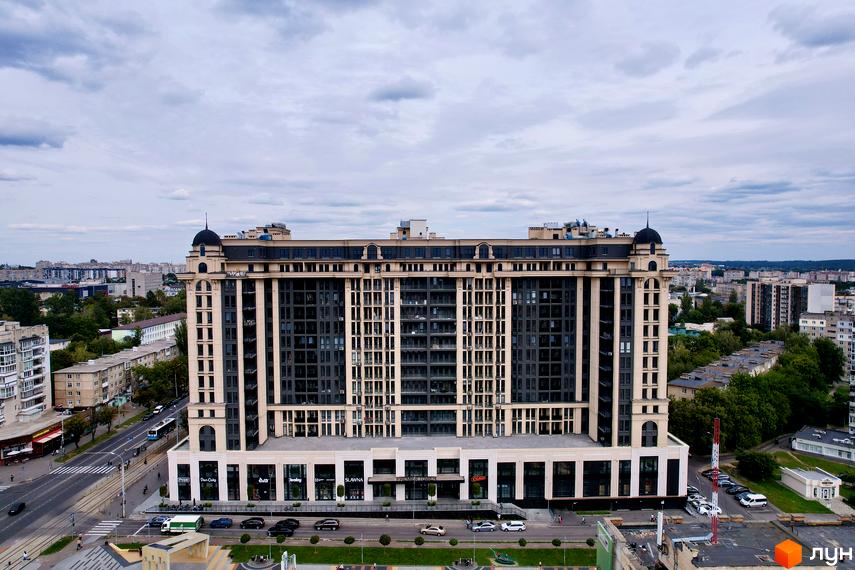 Житловий комплекс Premier Tower: багатоповерхова будівля з бежевим та темним фасадом, розташована біля дороги з транспортом та зеленими насадженнями.