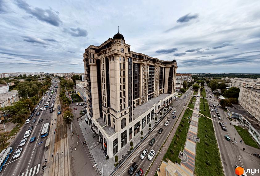 Висотна будівля ЖК Premier Tower з великими вікнами та світлим фасадом. Навколо будинку розташовані дороги з автомобілями та зелені насадження.