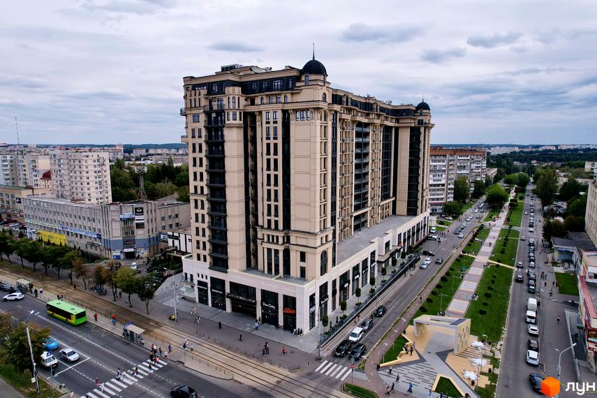 Житловий комплекс Premier Tower з бежевим фасадом, темними вікнами та купольними елементами. Поруч широка вулиця з трамвайними коліями та зеленими насадженнями.