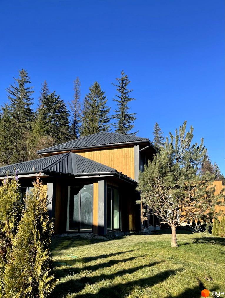 Будинок Котеджного містечка Агат Резорт & SPA з дерев'яними фасадами та темним дахом, оточений зеленим газоном та хвойними деревами.