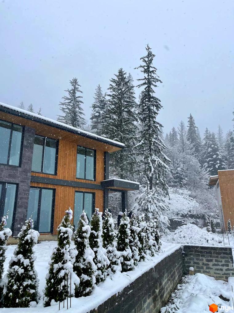 Котеджне містечко КМ Агат Резорт & SPA взимку. Будинок з дерев'яним фасадом та великими вікнами, навколо засніжені ялини та дерева.