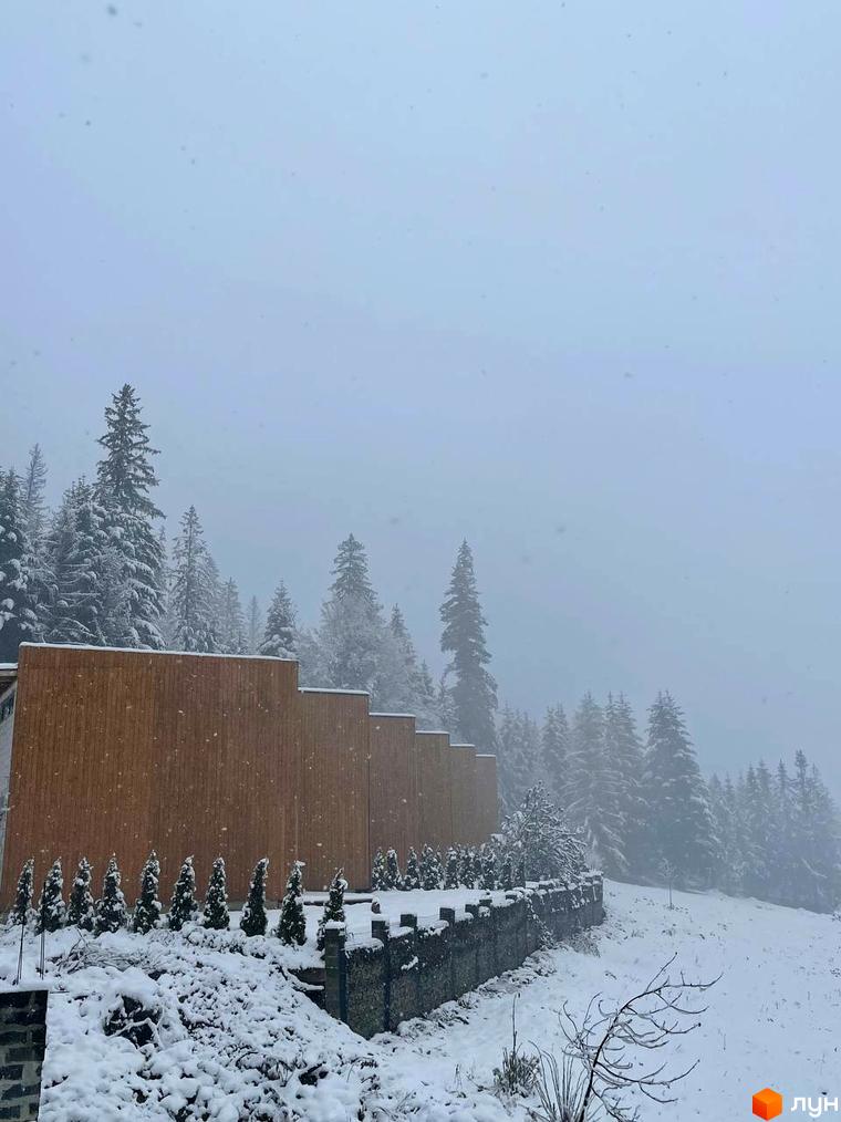 Котеджне містечко Агат Резорт & SPA взимку під час снігопаду, з дерев'яним фасадом будівлі та засніженою прибудинковою територією.