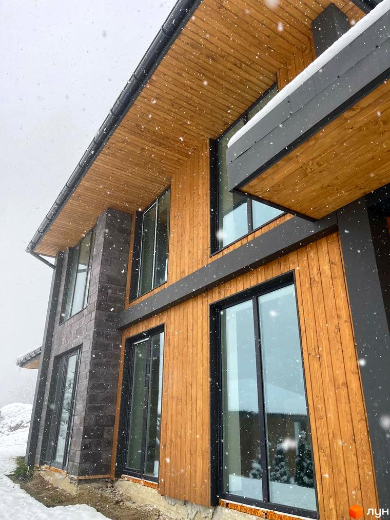 Котеджне містечко КМ Агат Резорт & SPA. Зовнішній вигляд будинку з дерев'яною обшивкою та темними елементами на тлі снігопаду.