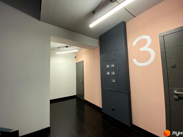 Клубний будинок „Васильченка“: двері з номером 7 та великою цифрою 3 на персиковій стіні. Сучасний коридор з двома дверима та освітленням.