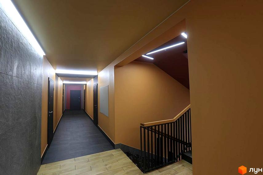 Інтер'єр коридору в Житловому комплексі Новатор з дверима та сходами. Освітлення забезпечують лінійні світильники на стелі.