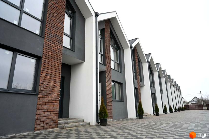 Ряд таунхаусів Dream Home з фасадами темно-сірого, білого кольорів та цегляними вставками. Перед будинками вимощена бруківка.