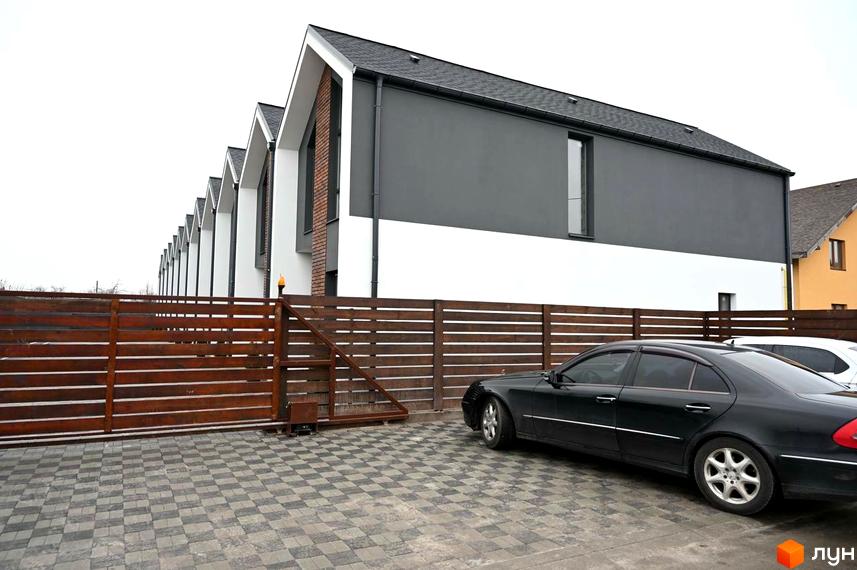 Таунхауси Dream Home: ряд будинків з темними дахами та двоколірними фасадами, перед якими розташований дерев'яний паркан та брукований двір.