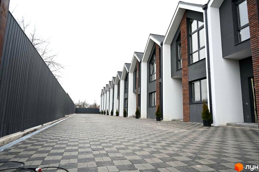 Ряд таунхаусів Таунхауси Dream Home з білими та темно-сірими фасадами, цегляними елементами. Прибудинкова територія викладена бруківкою, поруч високий паркан.