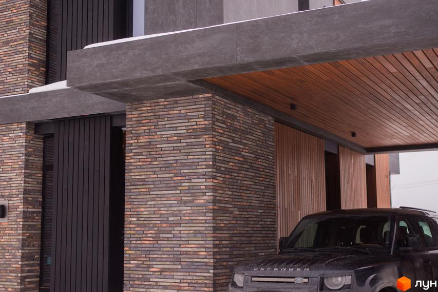 КМ 9 ЕЛЕМЕНТІВ: фасади будівель оздоблені цеглою та дерев'яними панелями, поруч припаркований автомобіль.
