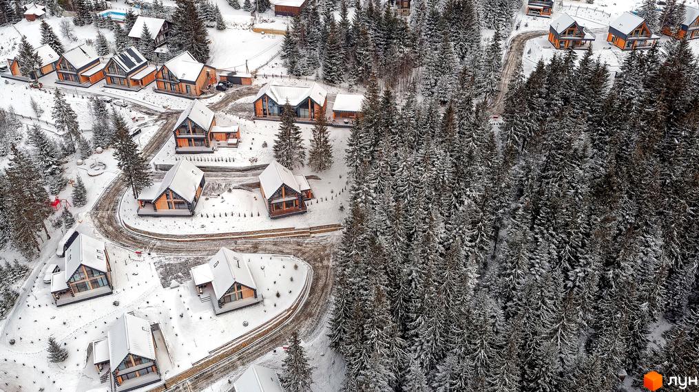 Зимовий вид на Котеджне містечко SKOGUR з дерев'яними котеджами та засніженою територією. Будинки з великими вікнами серед хвойного лісу.