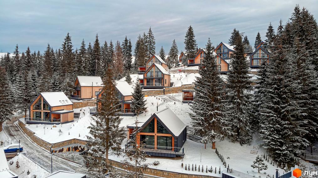 Зимовий пейзаж Котеджного містечка SKOGUR: дерев'яні котеджі з великими вікнами серед засніжених сосен. Затишне житло в гармонії з природою.